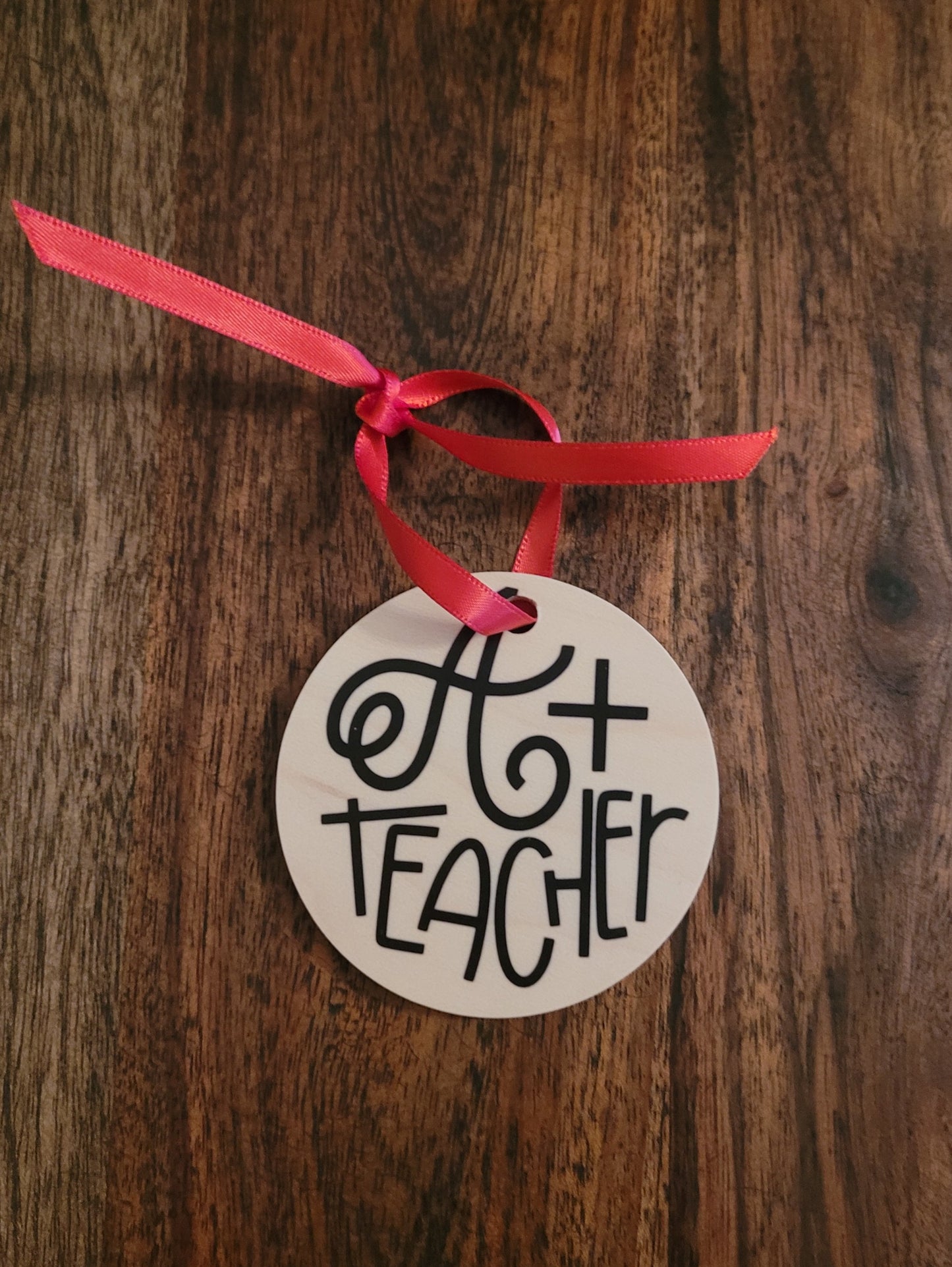 Circular wooden holiday ornament.  Says " A+ Teacher ".  Has a red ribbon tie for hanging.